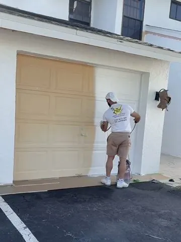Matias painting a garage door on a job site in an MS Painting Plus shirt